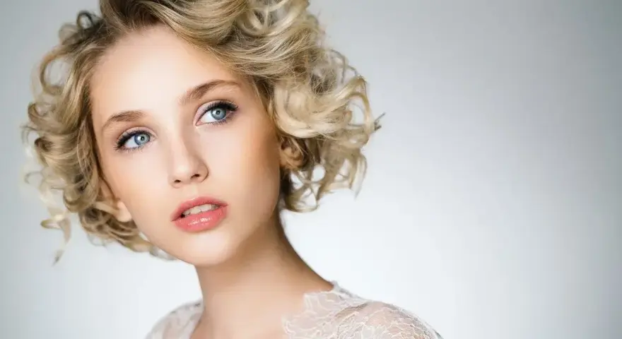 Blondynka z błękitnymi oczami i kręconymi włosami, prezentująca subtelny makijaż smoky eyes.