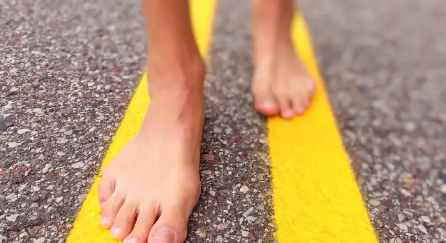 Piedi nudi che camminano su una strada con strisce gialle. Un'esperienza di correre scalzi per sentire la strada.