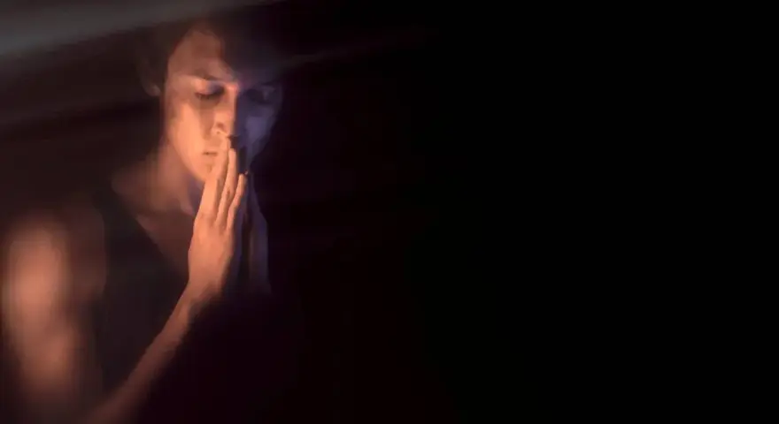 Młody mężczyzna w półmroku, z dłońmi złożonymi jak do modlitwy, szuka spokoju. Kiedy onanizm nie jest grzechem, a drogą do samopoznania.
