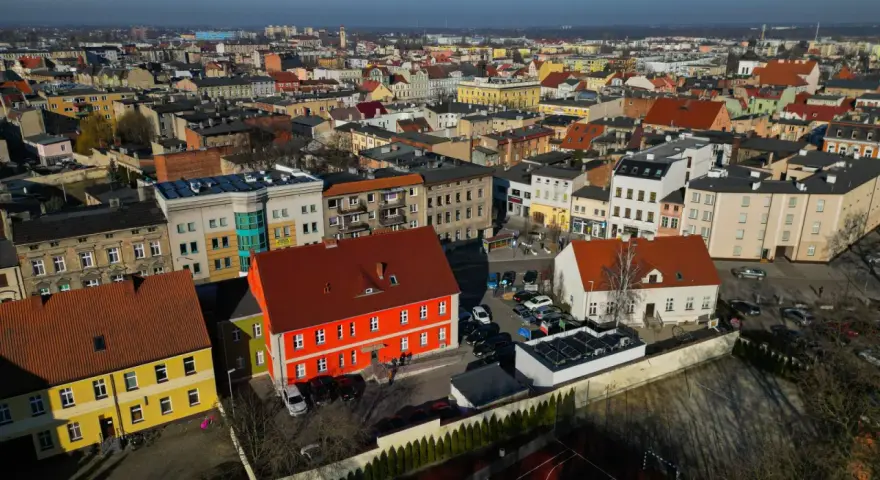 Widok z lotu ptaka na miasto, gdzie leży Ostrów Wielkopolski. Widać kolorowe kamienice, dachy i samochody.