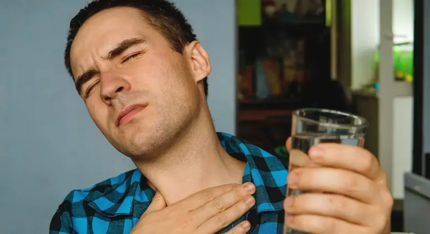 Mężczyzna z bólem gardła, cierpiący na nocny kaszel po alkoholu, sięga po szklankę wody.