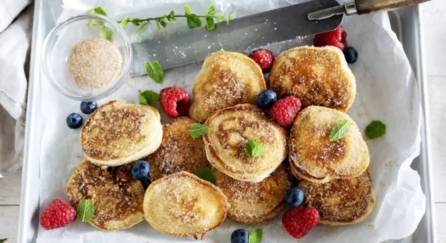 En bricka med nybakade krabbelurer, pudrade med socker och kanel, garnerade med färska bär och mynta. Perfekt för ett krabbelurer recept!