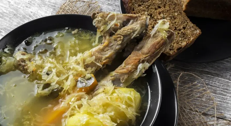 Kapuśniak ze świeżej kapusty czy kwaśnica? Aromatyczna zupa z żeberkami, ziemniakami i kiszoną kapustą, podana z ciemnym chlebem.