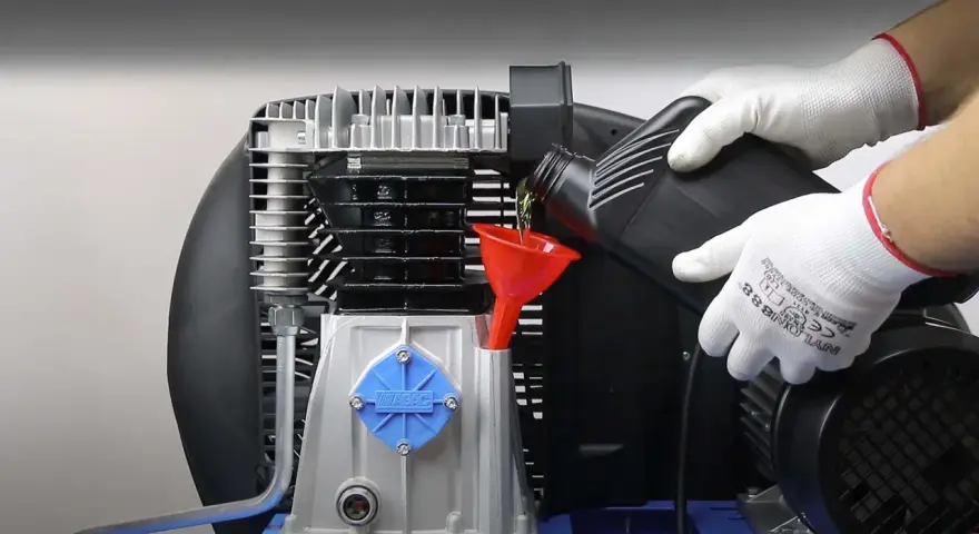 Wymiana oleju w sprężarce powietrza to kluczowy element jej naprawy. Ręce w białych rękawiczkach wlewają olej przez czerwony lejek.