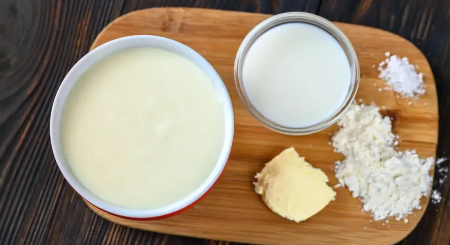 Zutaten für eine Mehlschwitze: Butter, Mehl, Milch und Salz auf einem Holzbrett.