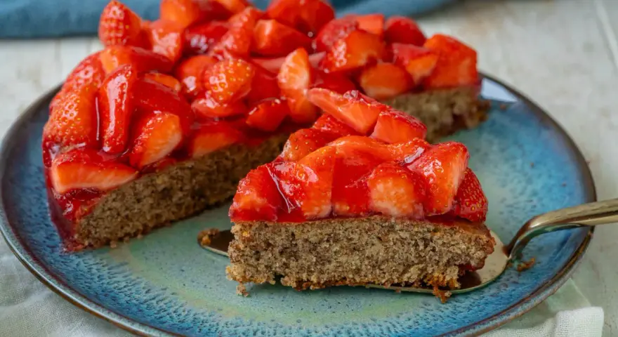 Ein saftiger glutenfreier Erdbeerkuchen mit frischen Erdbeeren und glänzender Tortenglasur auf einem blauen Teller.