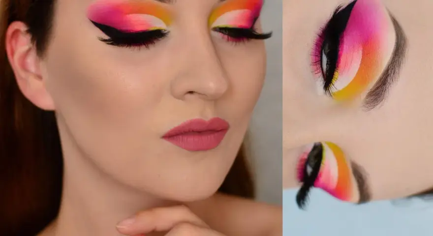 Oczy z wyrazistym makijażem cut crease w odcieniach różu, pomarańczy i żółci. Czarne kreski i długie rzęsy podkreślają spojrzenie.
