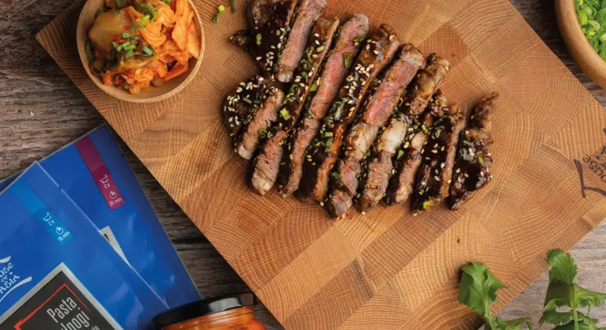 Pokrojony stek bulgogi polany sosem, obok miseczka z kimchi i opakowanie pasty do bulgogi.