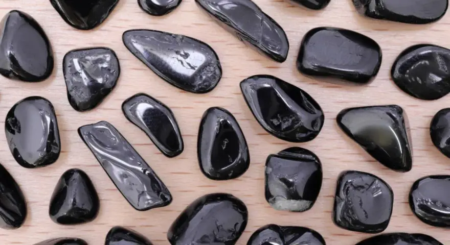 Tormalina nera, nota per le sue proprietà protettive e di radicamento, in una collezione di pietre levigate su fondo di legno.