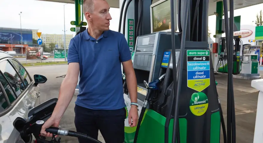 Mężczyzna dokonuje tankowania swojego samochodu na stacji paliw. W ręku trzyma pistolet do paliwa, gotowy do rozpoczęcia procesu.