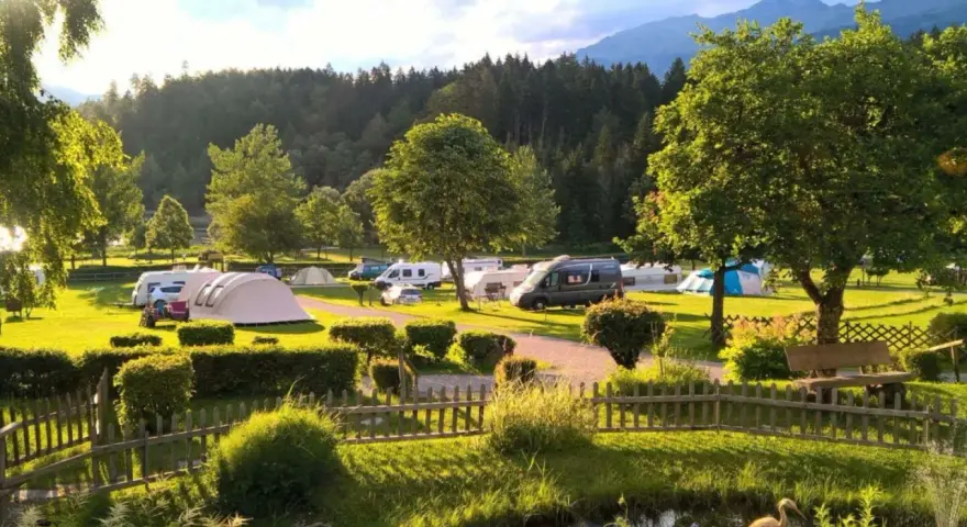 Idyllischer Campingplatz in den Dolomiten mit Wohnmobilen, Zelten und einem Teich.