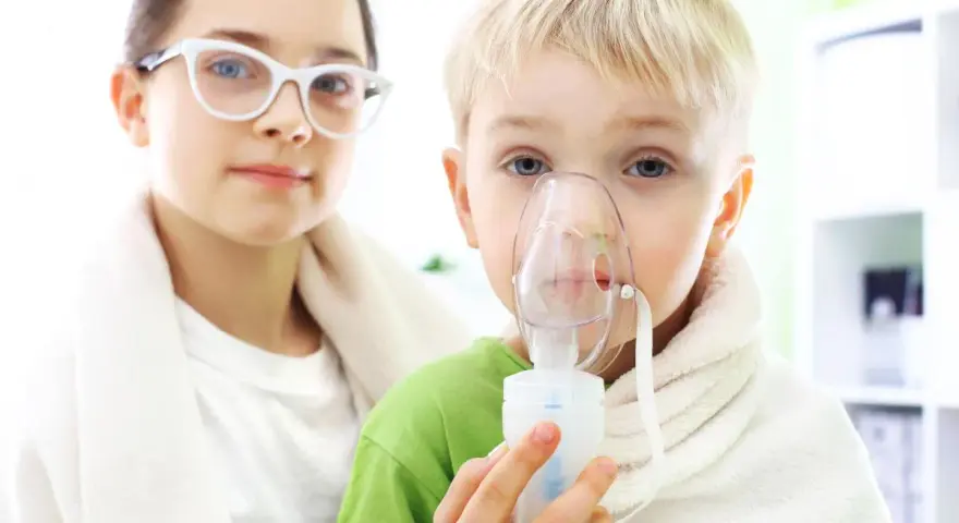 Dziecko z maską inhalatora, obok dziewczynka w okularach.