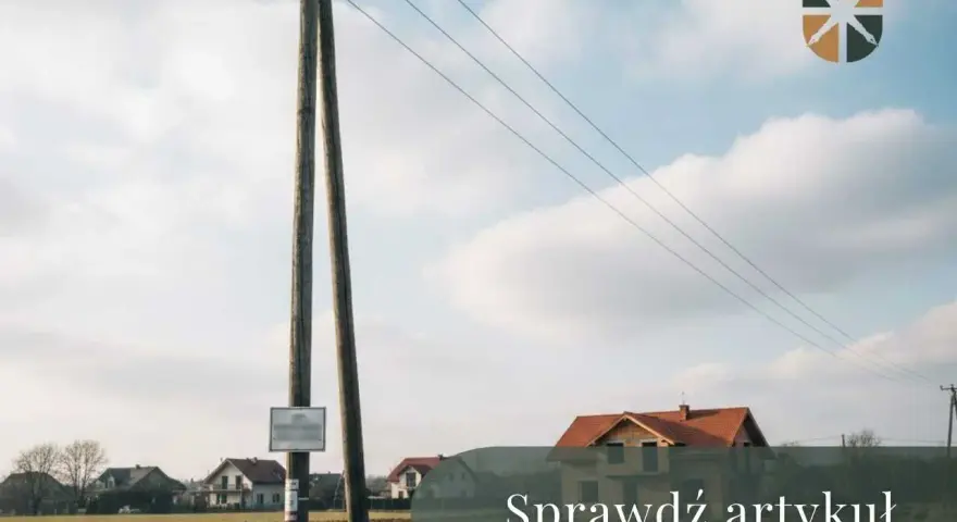 Drewniany słup z przewodami tworzy linię napowietrzną nad polami i domami.