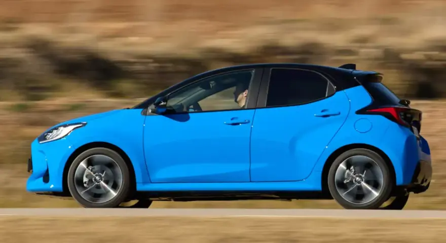 Niebieski hatchback z czarnym dachem pędzi po drodze, za kierownicą siedzi mężczyzna.