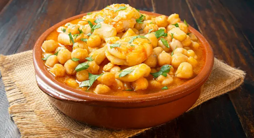 Un plato de barro con garbanzos y langostinos, adornado con perejil fresco, sobre una mesa de madera rústica.