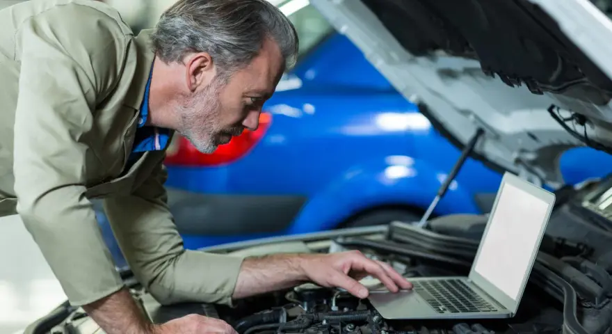 Mechanik z laptopem przy otwartej masce samochodu.