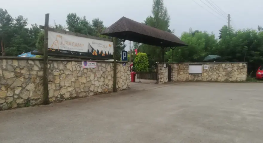 Wjazd na siamoszyce camping przez kamienny mur. Baner "Jura Camp" zaprasza do wypoczynku wśród drzew.
