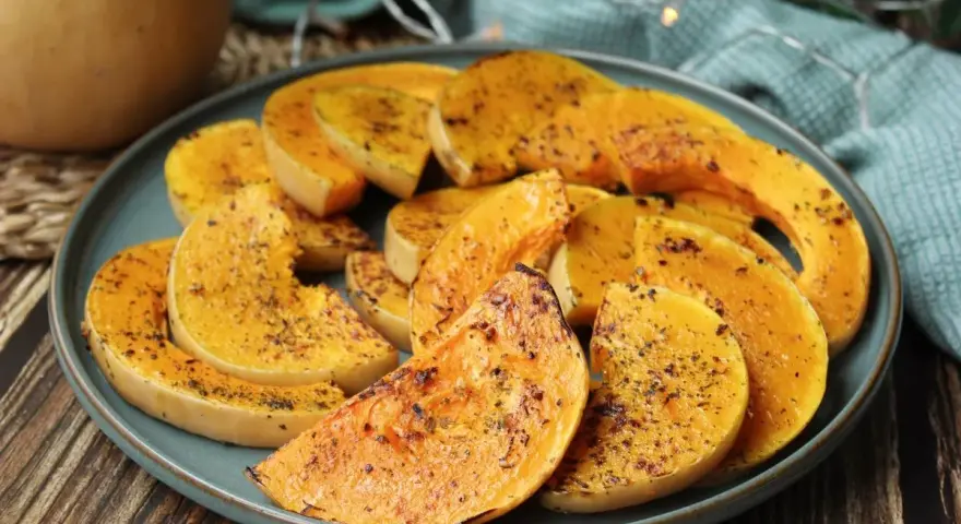 Rodajas de calabaza a la plancha, doradas y especiadas, servidas en un plato azul sobre una mesa de madera.