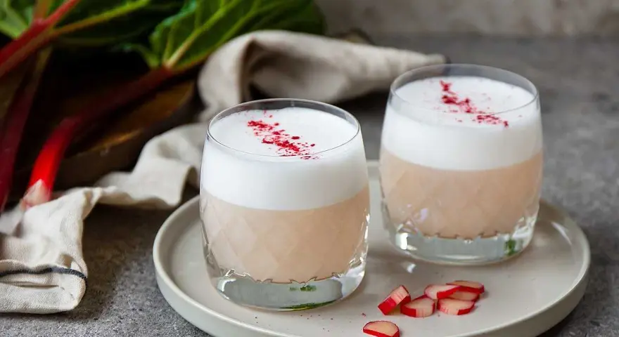 Två glas med rabarber sour, toppade med skum och strödd rabarberpulver. En härlig syrlig sommardröm.