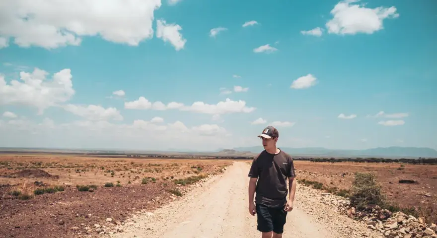 Ein junger Mann mit Kappe geht auf einer staubigen Straße in der afrikanischen Savanne. Ein bezahltes Praktikum im Ausland nach dem Abitur ist ein Abenteuer.