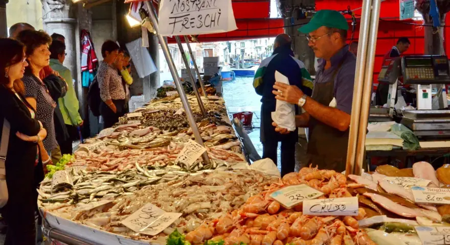 Mercato del pesce a Venezia: bancarelle piene di pesce fresco, gamberi e calamari. Un venditore serve i clienti.