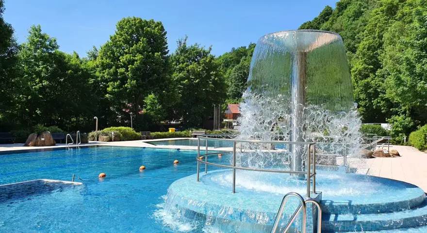 Erfrischender Brunnen im Naturbad Elbingerode, umgeben von grünen Bäumen und blauem Wasser.