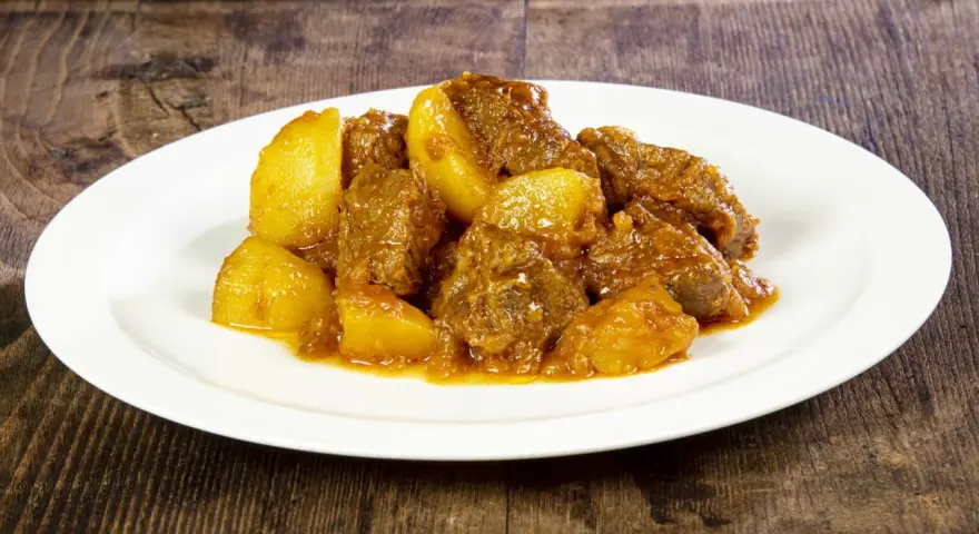 Un saporito spezzatino di vitello con patate, servito su un piatto bianco, su uno sfondo di legno scuro.