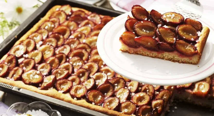 Ein saftiger Zwetschgenkuchen vom Blech, mit süßen Früchten und Zucker bestreut, wartet darauf, genossen zu werden.