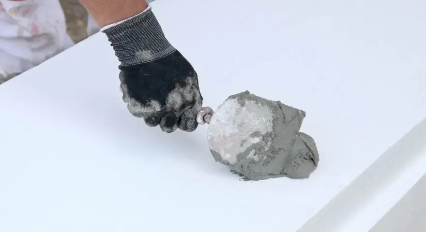 Ręka w rękawicy nakłada zaprawę na styropian. To pokazuje, jaki klej do styropianu wybrać do prac termoizolacyjnych.