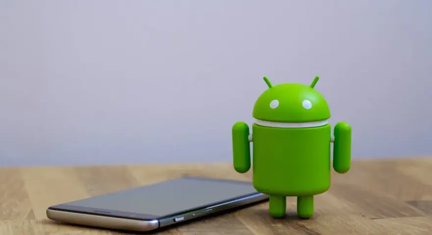 Zielony robot Android obok telefonu, symbolizujący najnowszą wersję systemu android 14.