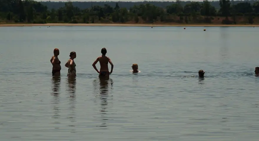 Menschen genießen das naturbad luppa an einem sonnigen Tag. Einige stehen im Wasser, andere schwimmen.