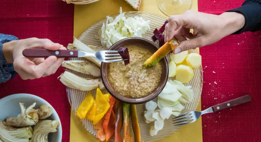 Un gruppo di mani intinge verdure nella bagna cauda, un piatto conviviale.