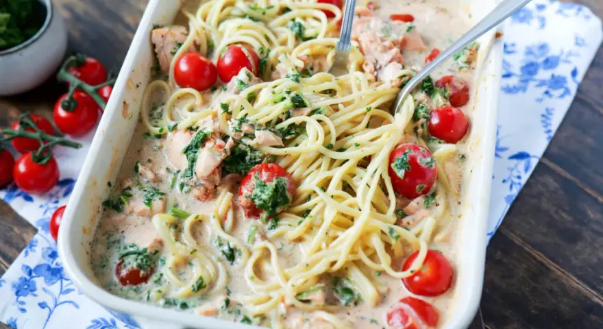 Cremige Lachs Spinat Pasta mit Kirschtomaten in einer Auflaufform, serviert mit zwei Gabeln.