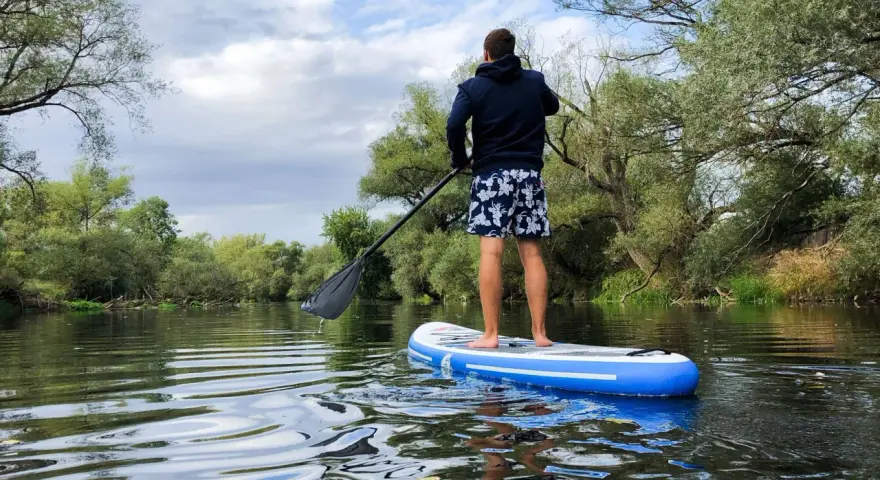 Mann auf SUP-Tour auf einem ruhigen Fluss, umgeben von üppiger Vegetation.