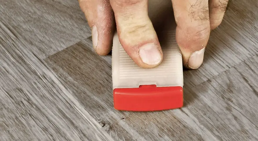 Fingrar använder en kil för att laga laminatgolv.