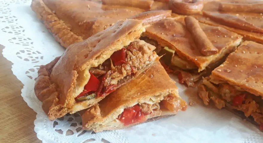 Una deliciosa empanada de carne, cortada en porciones, revela su jugoso relleno de carne deshebrada y pimientos rojos.
