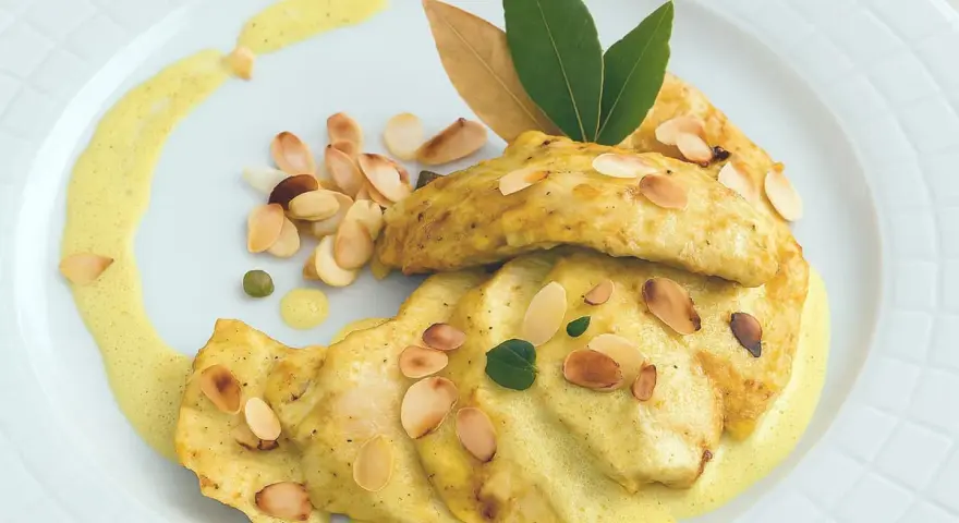 Délicieux poulet au curry, garni d'amandes effilées et d'une sauce onctueuse, servi sur une assiette blanche.