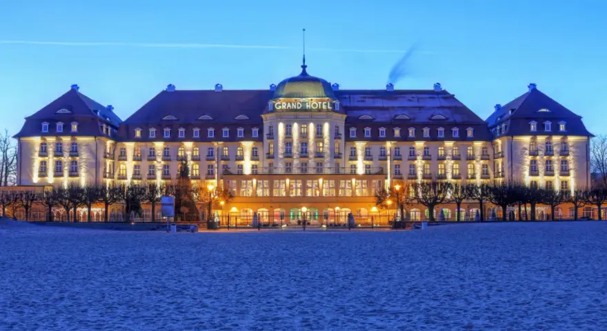Elegancki Grand Hotel, część sieci luksusowych hoteli, lśni nocą na tle plaży.