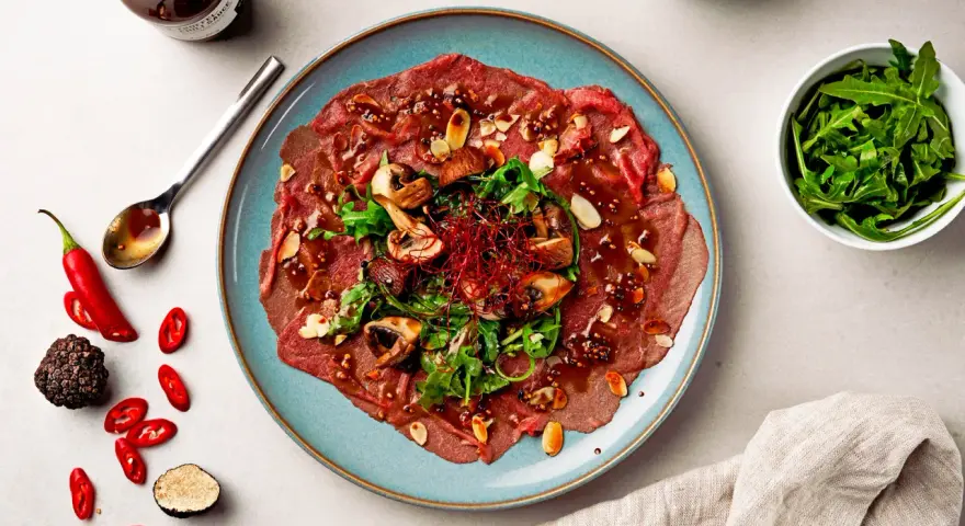Carpaccio vom Rind mit Pilzen, Rucola und Mandeln, garniert mit Chili und Trüffel. Ein Gericht, das zeigt, was ist Carpaccio.