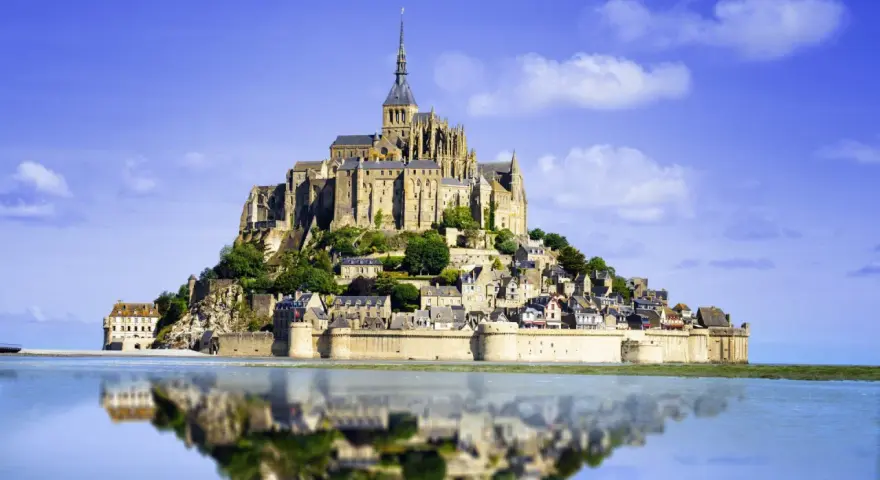 Opactwo Mont Saint-Michel, jeden z najpiękniejszych miejsc we Francji, odbija się w spokojnej wodzie.
