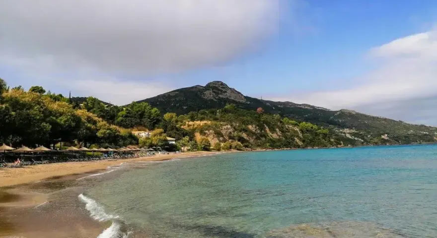 Piękna plaża Tragaki Zakynthos z turkusową wodą, zielonymi wzgórzami i rzędem leżaków pod parasolami.