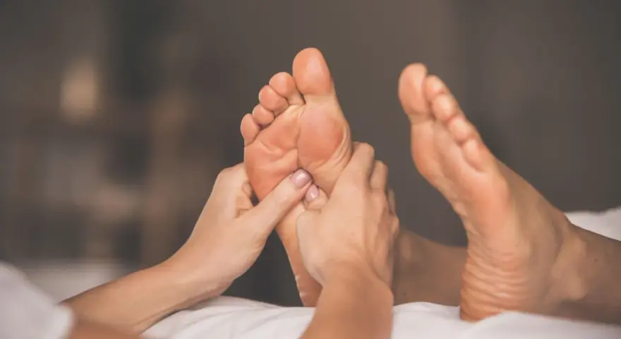 Hands giving a relaxing foot rub to a person lying on a white surface.
