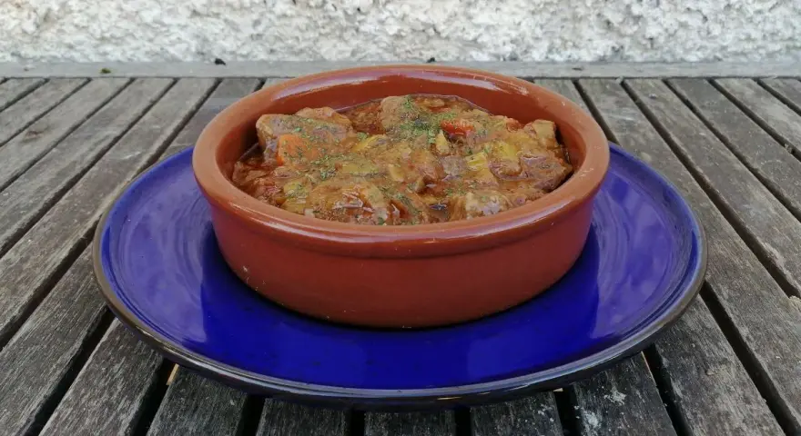 Goulash de ternera humeante en cazuela de barro, servido sobre plato azul. Un plato reconfortante listo para disfrutar.