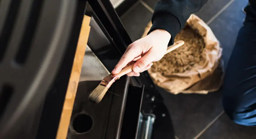 Mano che pulisce la stufa a pellet con un pennello. La manutenzione stufa a pellet ogni quanto è fondamentale per l'efficienza.