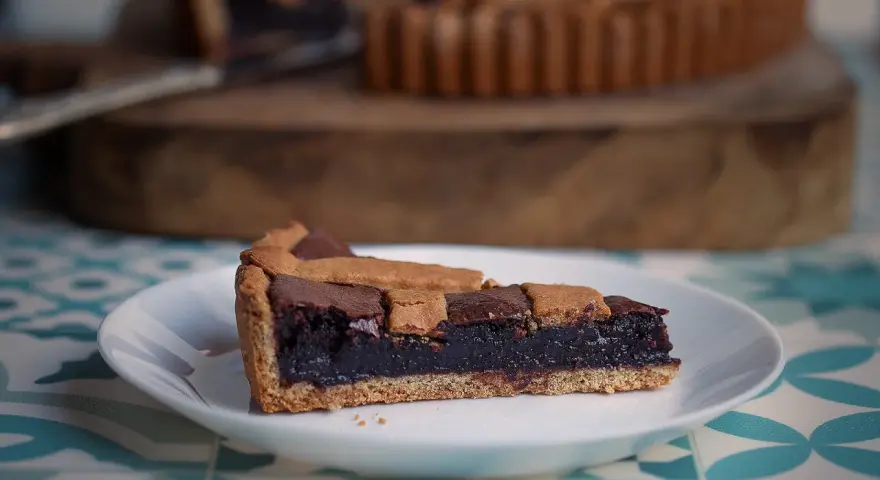 Una fetta di crostata al cioccolato, con la sua base dorata e il ripieno scuro e invitante, pronta per essere gustata.