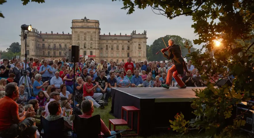 Ein Geiger spielt auf einer Bühne vor einem Schloss, während ein Publikum zusieht. Ein schönes Beispiel für Veranstaltungen an der Ostsee.