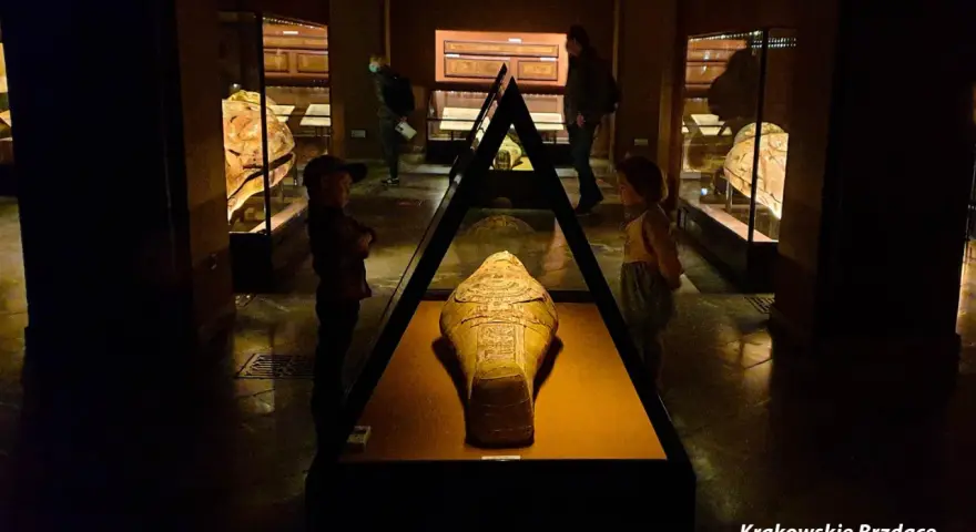 W muzeum archeologicznym w Krakowie dzieci oglądają starożytną mumię w sarkofagu.