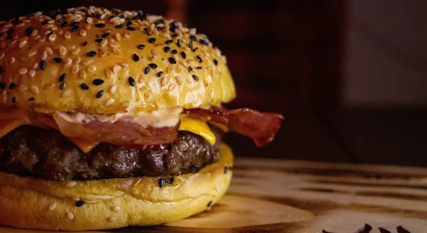 Soczysty burger z bekonem i serem na bułce z sezamem.