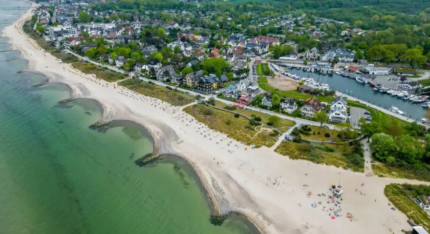 Luftaufnahme eines Strandes mit grüner Ostsee, Häusern und einem Yachthafen. Ein idyllischer Ort für ruhige Orte an der Ostsee.