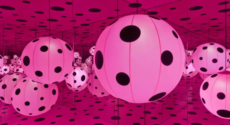 Salle infinie de Yayoi Kusama, remplie de sphères roses lumineuses à pois noirs, reflétées à l'infini par des miroirs.